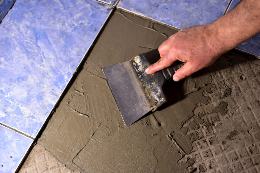 The hands of a man with a spatula apply the solution to the floor.